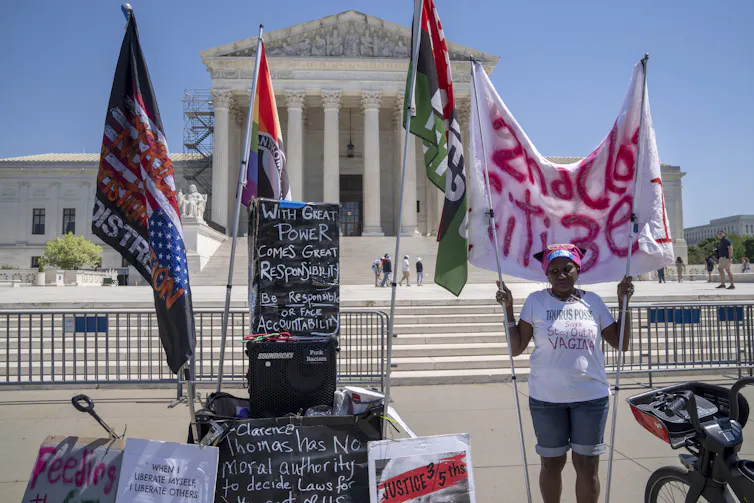 Woman outside the Supreme Court building holding an array of signs urging the Supreme Court to maintain access to telehealth abortion.