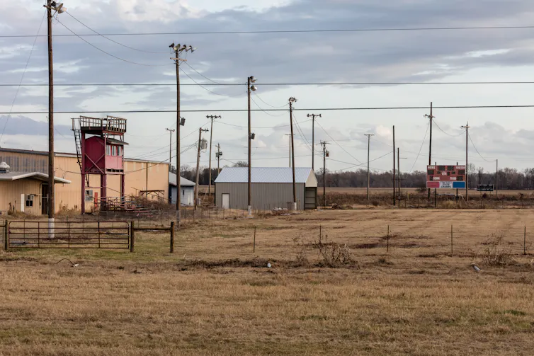 A scoreboard and old-looking building are seen in a brown field.
