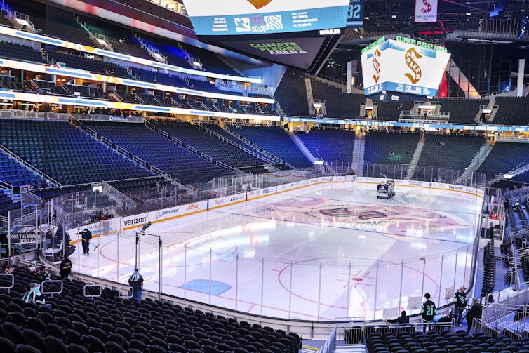 A view from the upper deck of a large hockey arena. Two Zambonis are cleaning the ice.