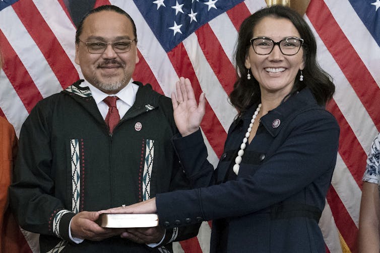 A woman smiles and places her left hand on a Bible held by a man.