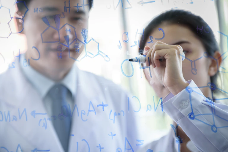 man and woman in white coats write chemical formulas with marker on clear glass