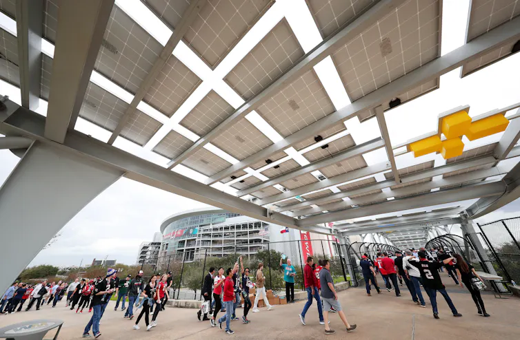 People walk under a canopy with solar panels above.