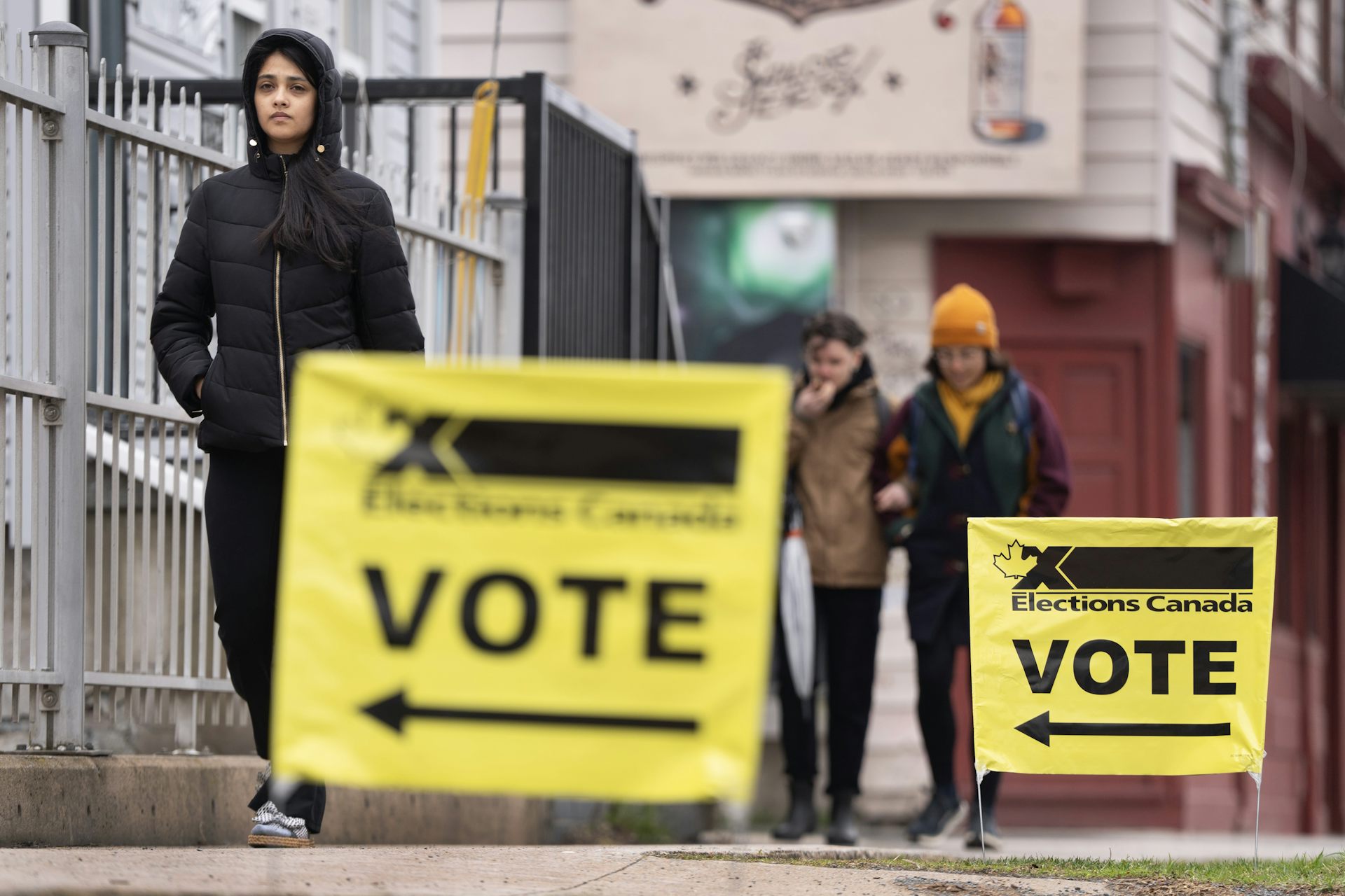  A young person in a hooded jacket next to a yellow vote sign.