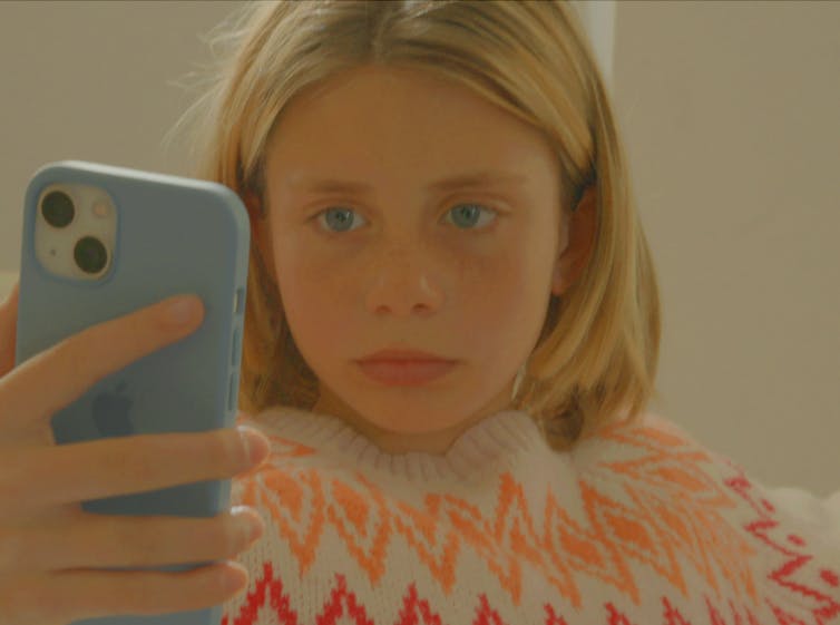 A young girl looks at a mobile phone screen.