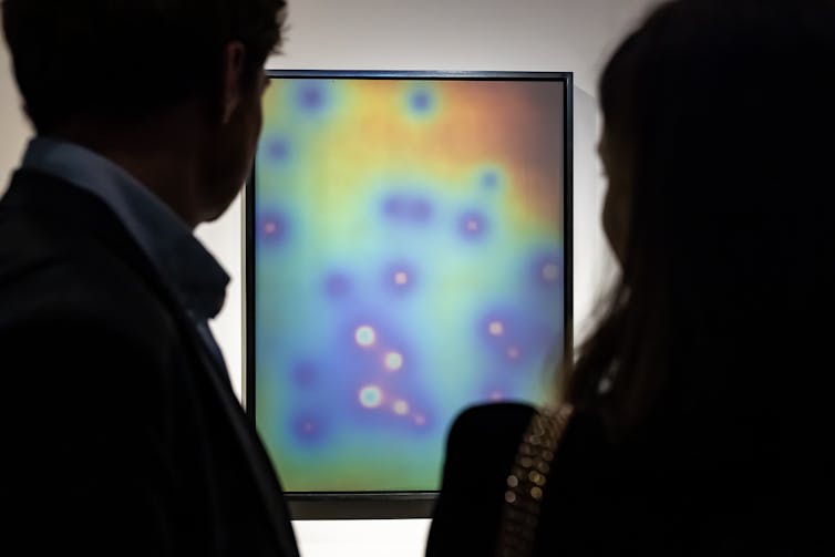 Two people look at a multi-coloured neon print.