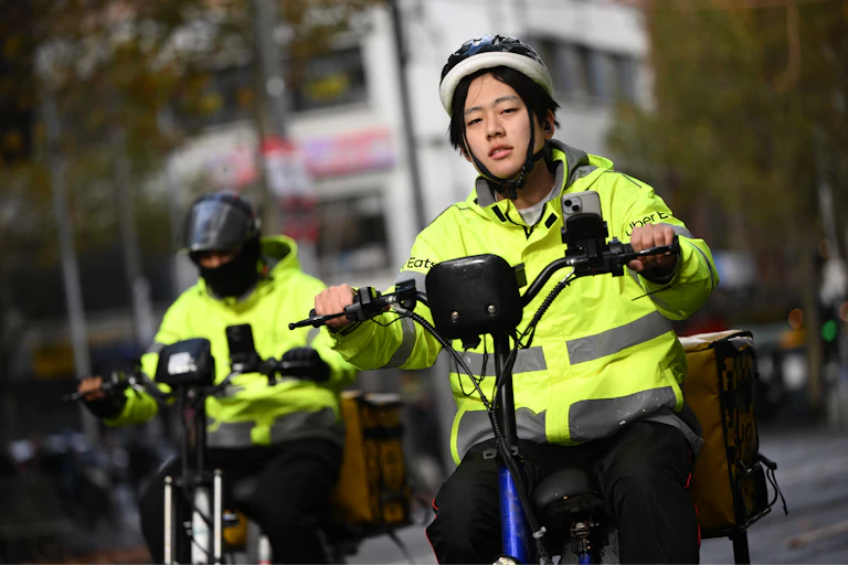 Two delivery riders on bikes wearing Uber Eats high vis jackets.