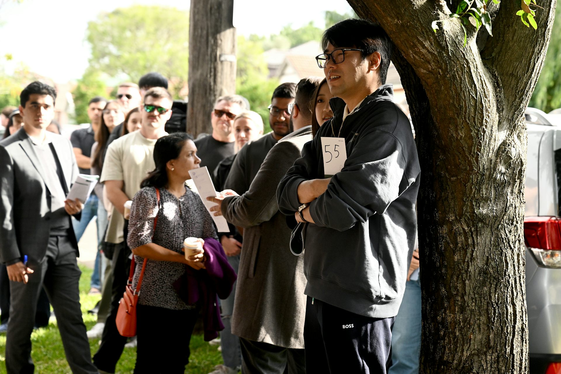 A crowd of people on a residential street holding numbers for a property auction