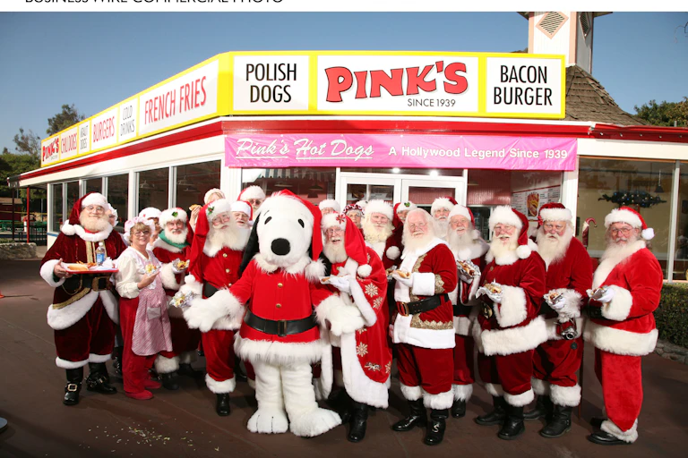 A group of Santas, including a Snoopy Santa, pose for a photo in front of a rural restaurant.