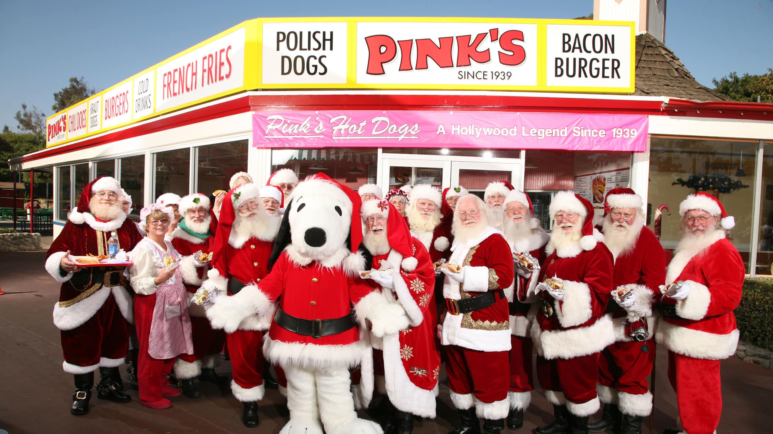 A group of Santas, including a Snoopy Santa, pose for a photo in front of a rural restaurant.