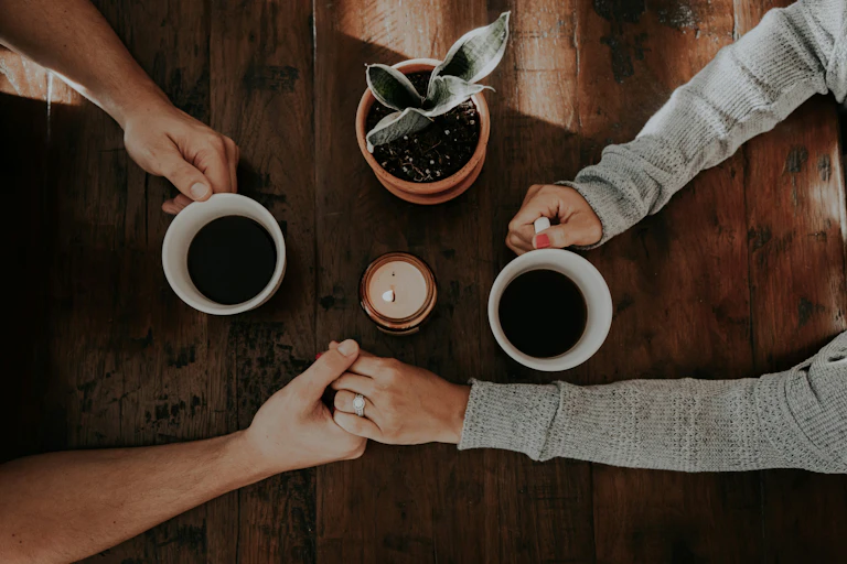 Man and women holding hands across table holding coffee cups