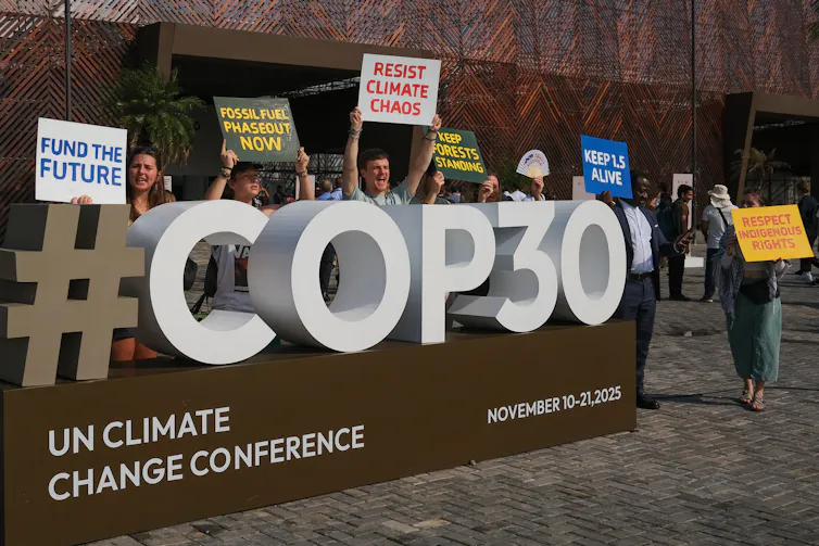 People holding protest signs demanding climate action in front of the COP30 sign