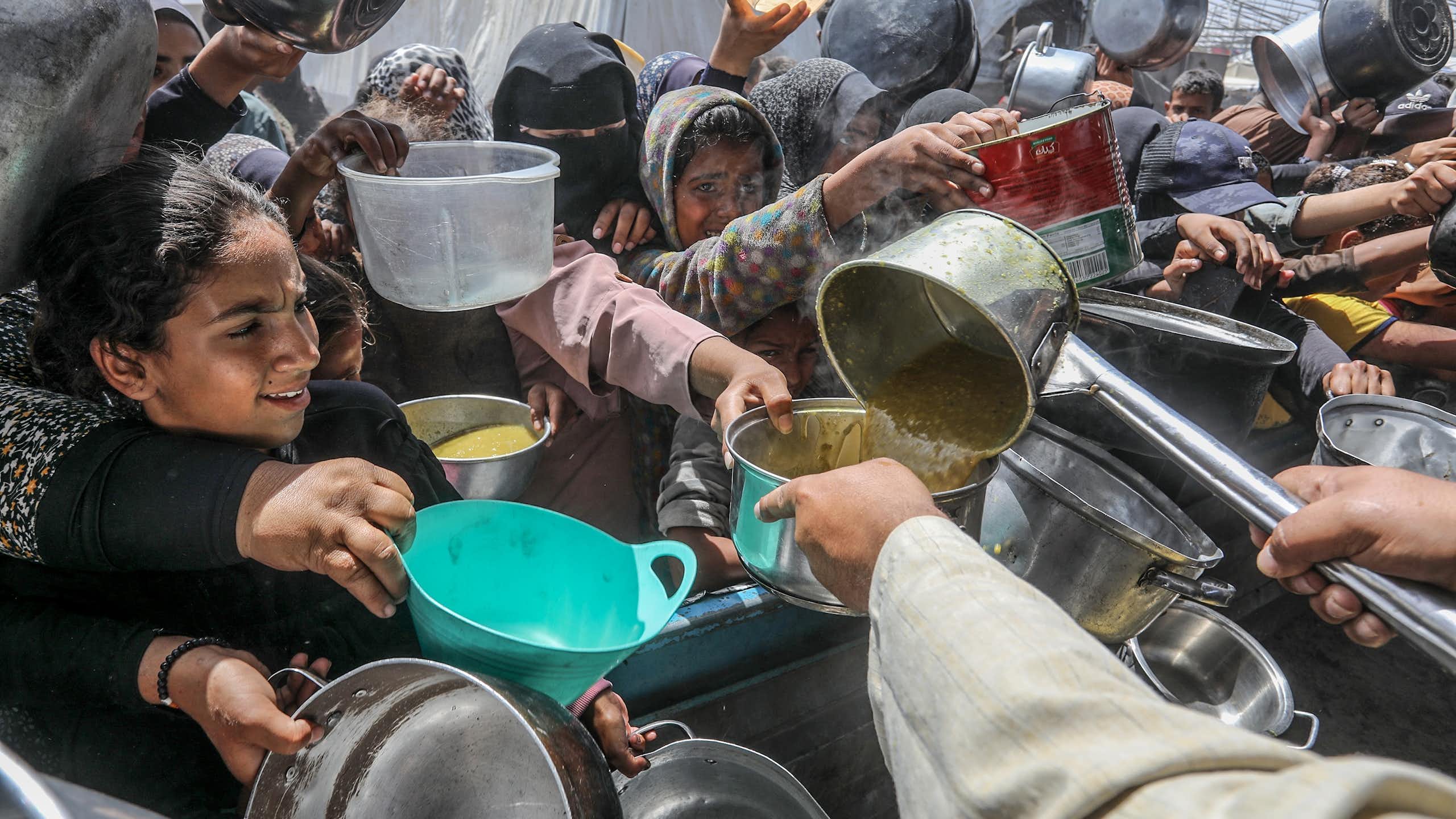 A crowd of people with pots, pans and containers gather to receive food.