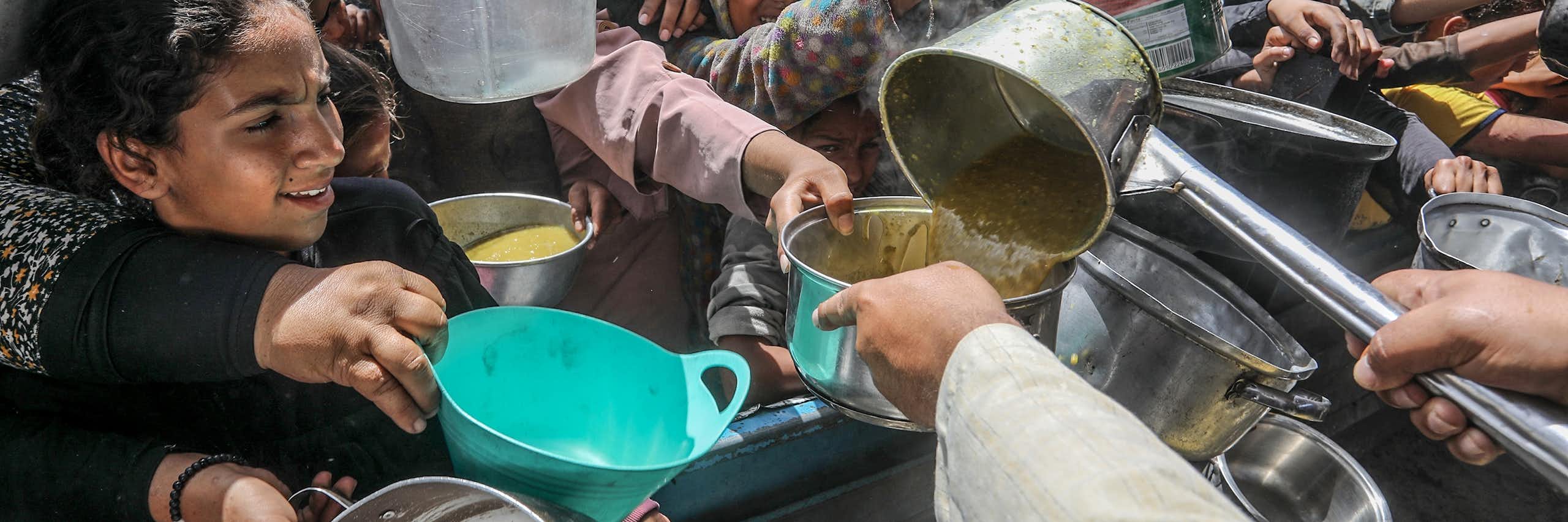 A crowd of people with pots, pans and containers gather to receive food.