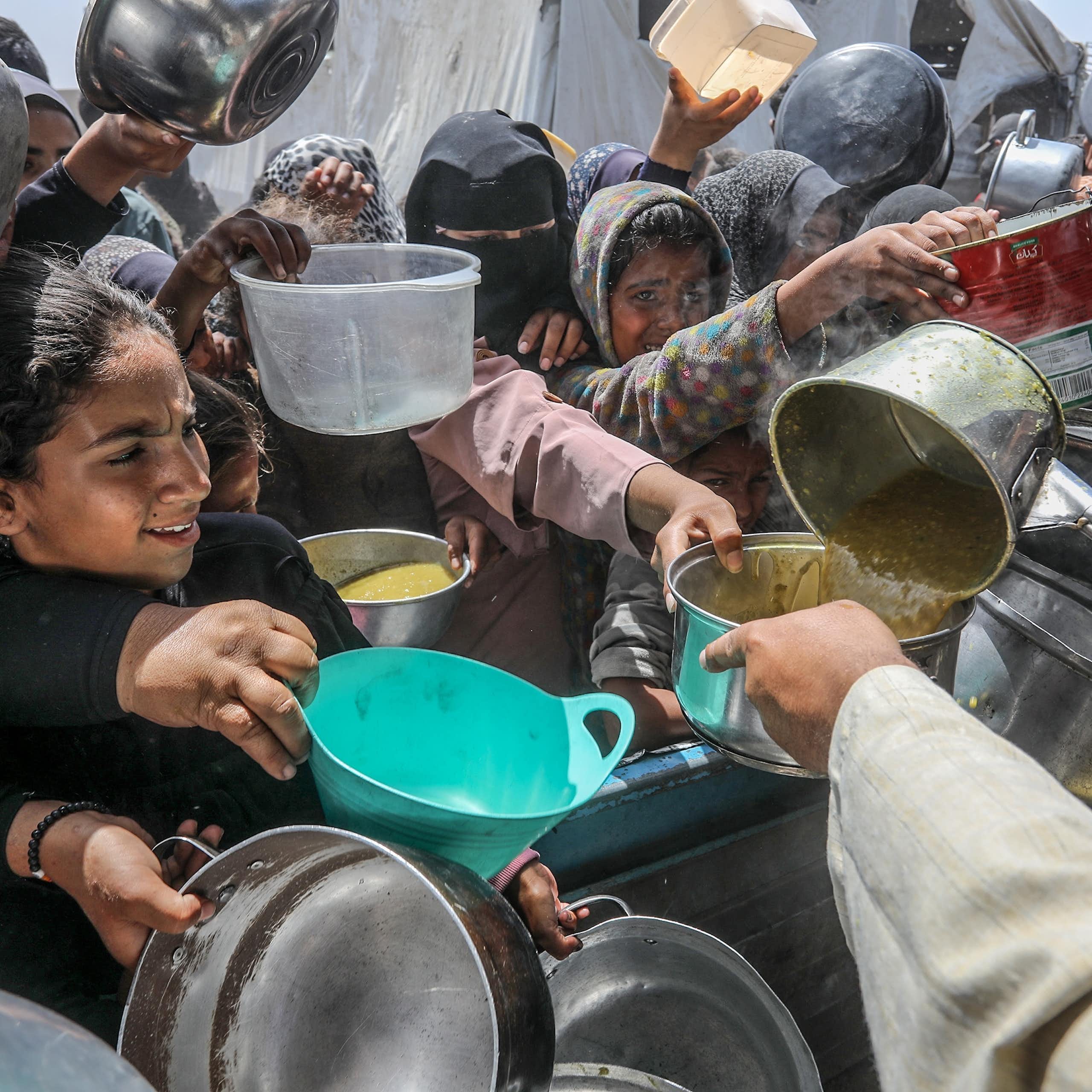 A crowd of people with pots, pans and containers gather to receive food.