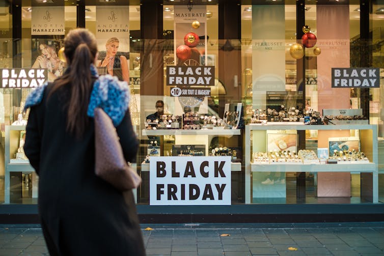 Woman standing in street looking at shopfront with black Friday promotion signs in the window.