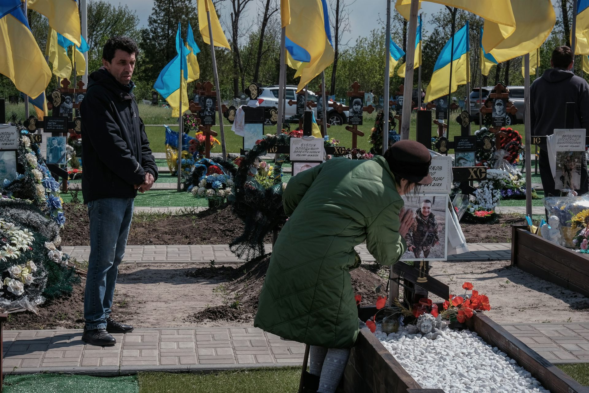 A woman tends a grave in a Ukrainian cemetery as a man looks on.