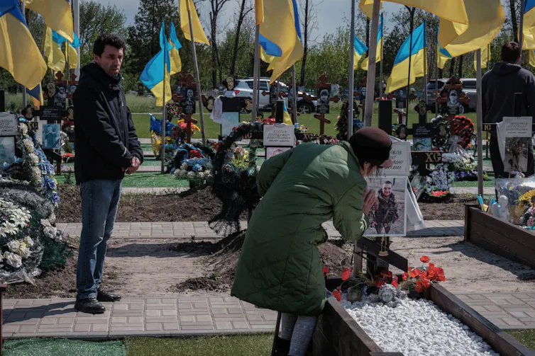 A woman tends a grave in a Ukrainian cemetery as a man looks on.