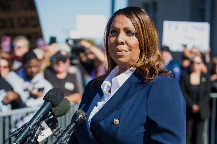A woman speaks outdoors in front of microphones.
