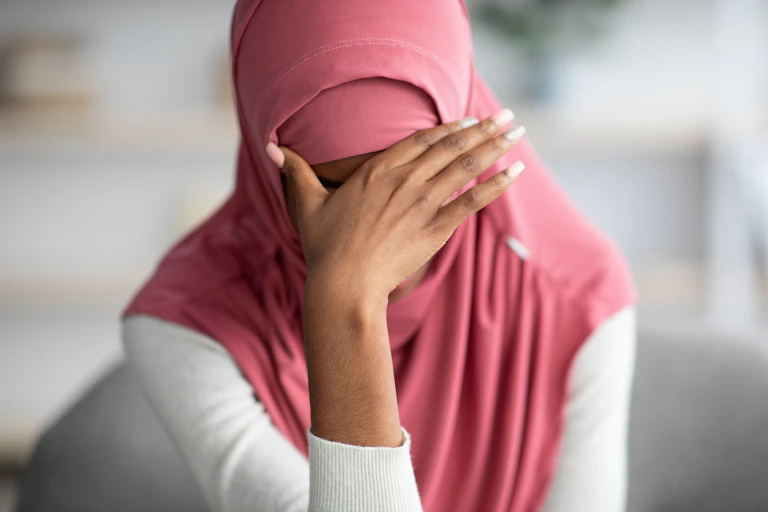 A woman in a hijab with her hand over her eyes