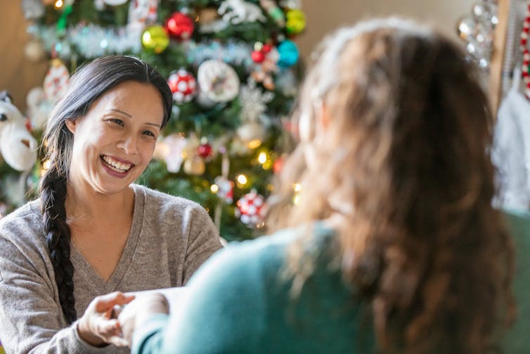 Una mujer se para frente a un árbol de Navidad y recibe un regalo.