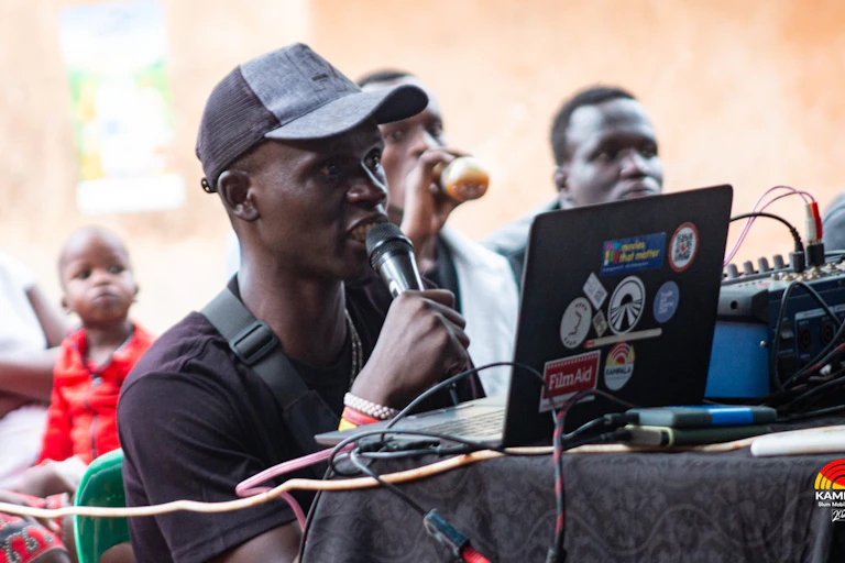 A man sits at a laptop with a microphone