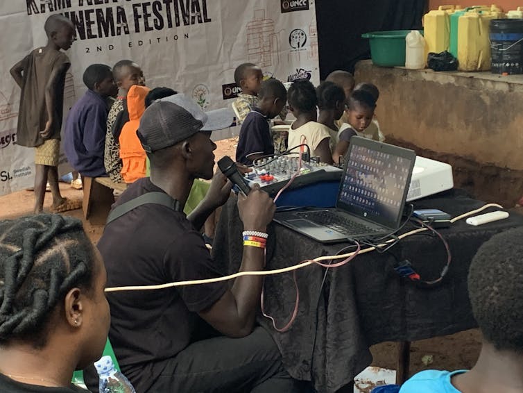 A man sits at a laptop with a microphone