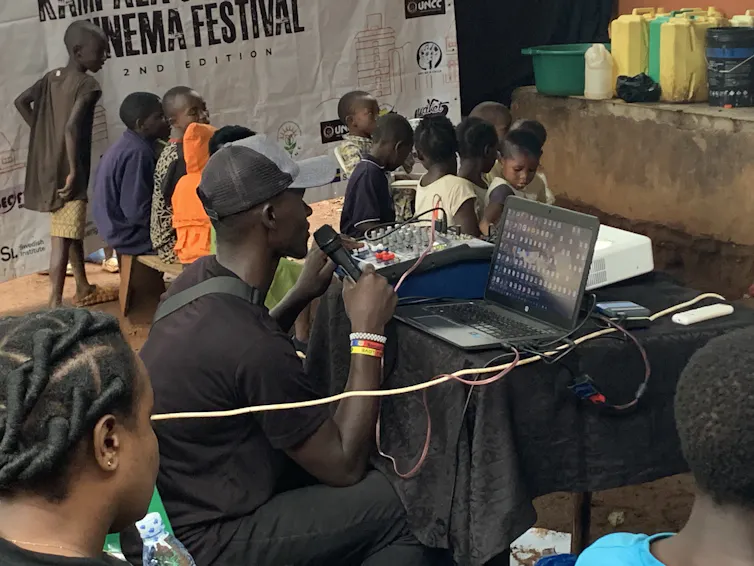 A man sits at a laptop with a microphone