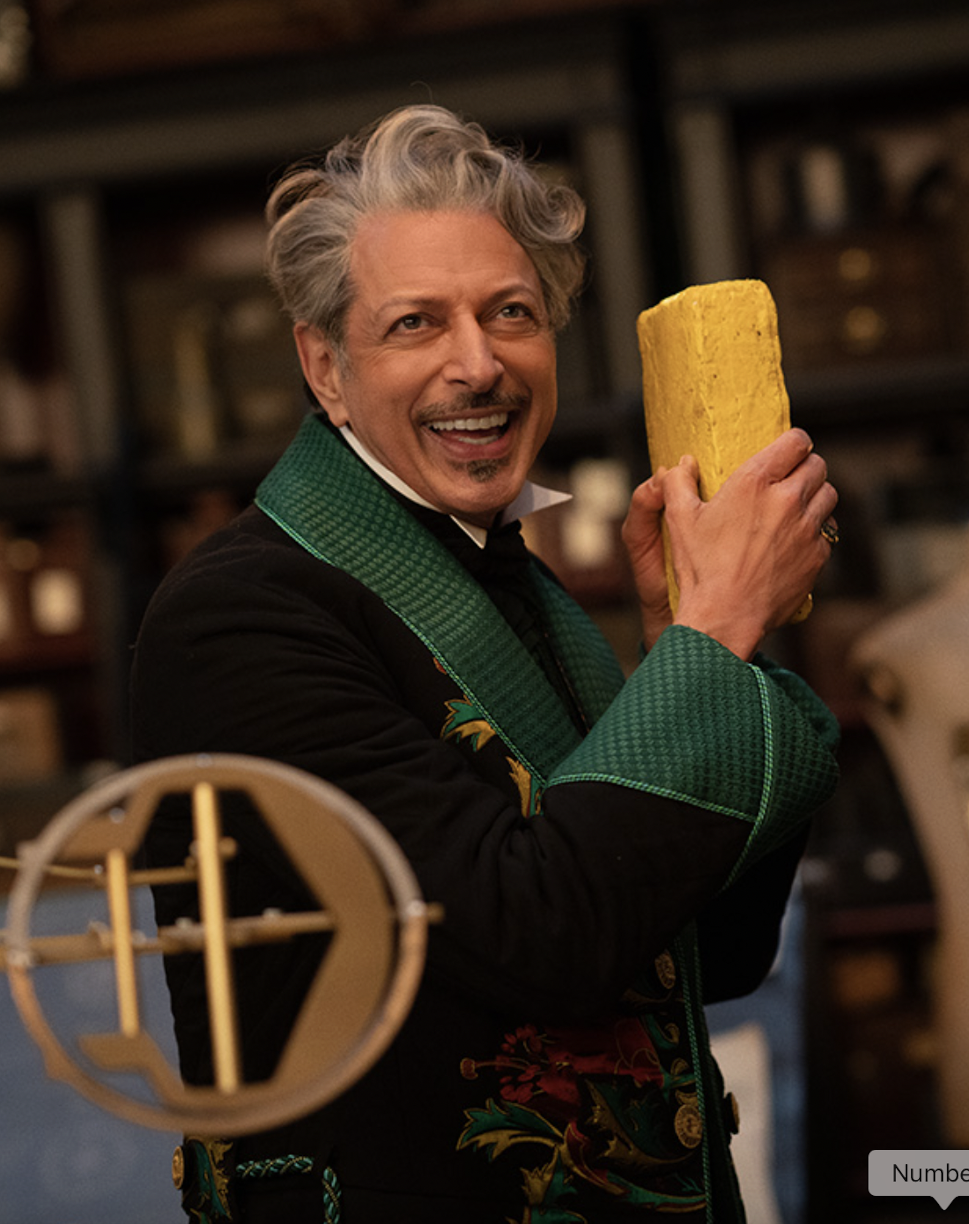 An older man in a fancy green suit holding a yellow brick in his hand.