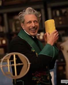 An older man in a fancy green suit holding a yellow brick in his hand.