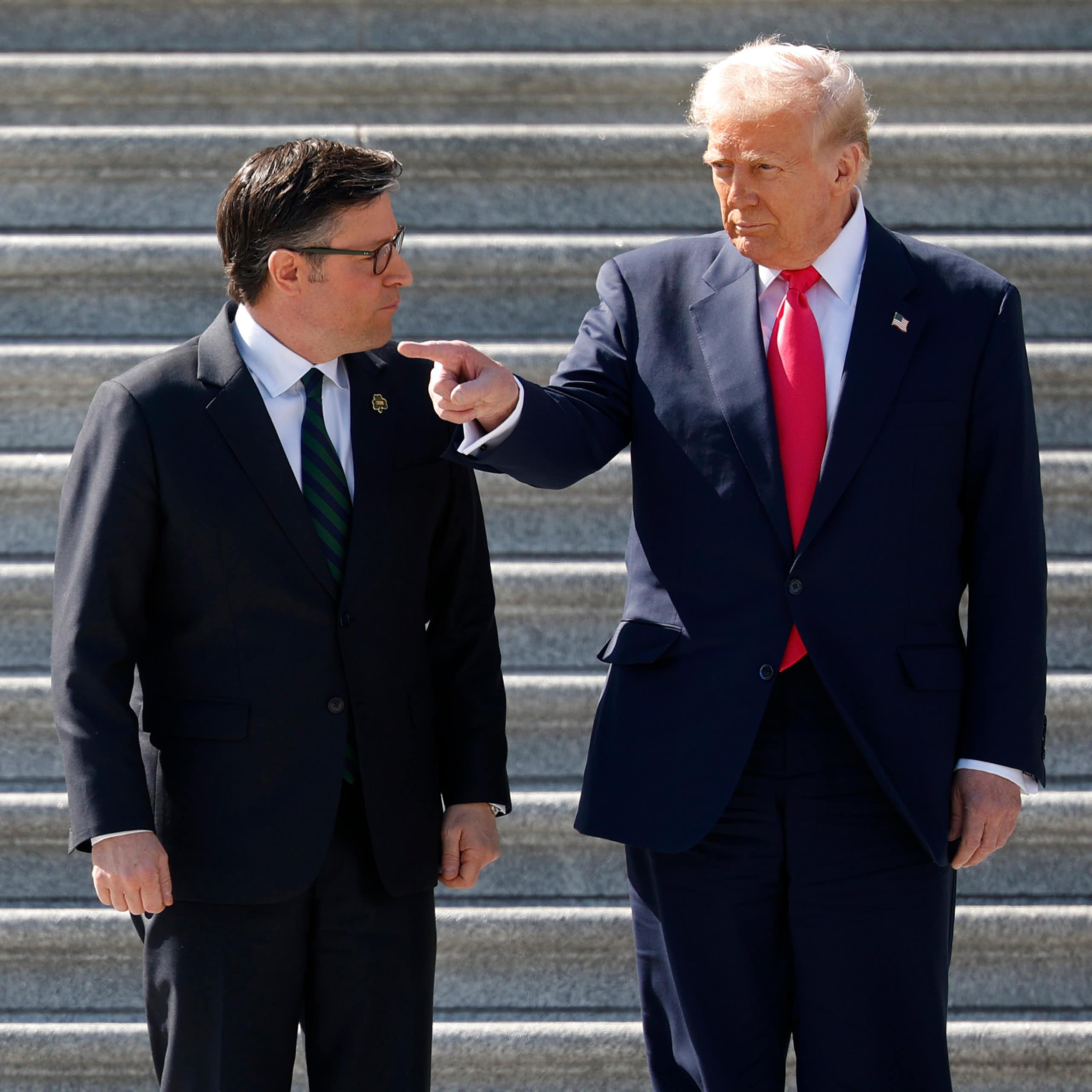 Two men in dark suits outside on stone stairs.