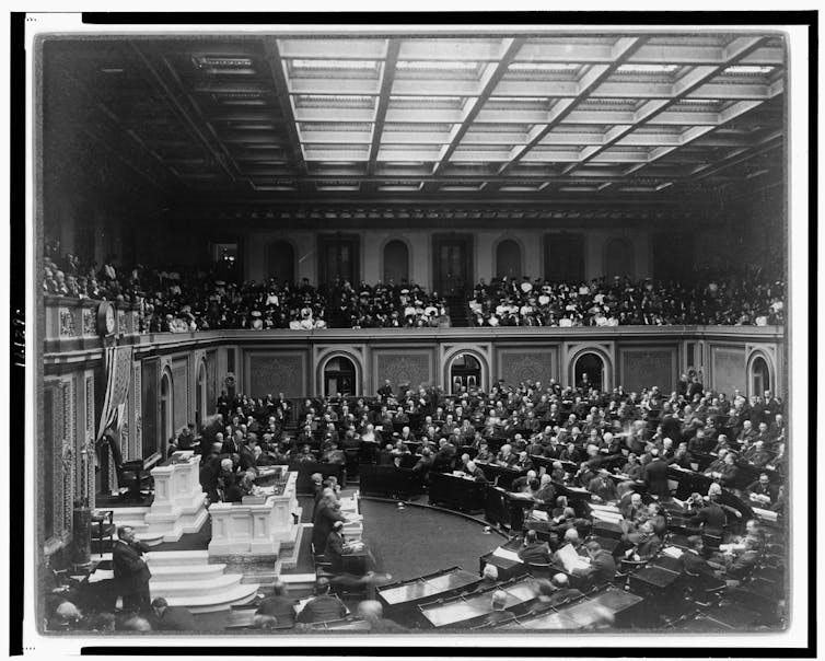 A large room with many people sitting in semicircular rows.