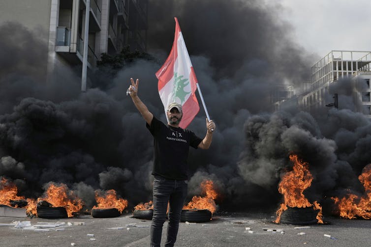 Un manifestante sostiene una bandera frente a neumáticos en llamas.
