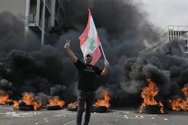 A protester holds a flag in front of burning tires.