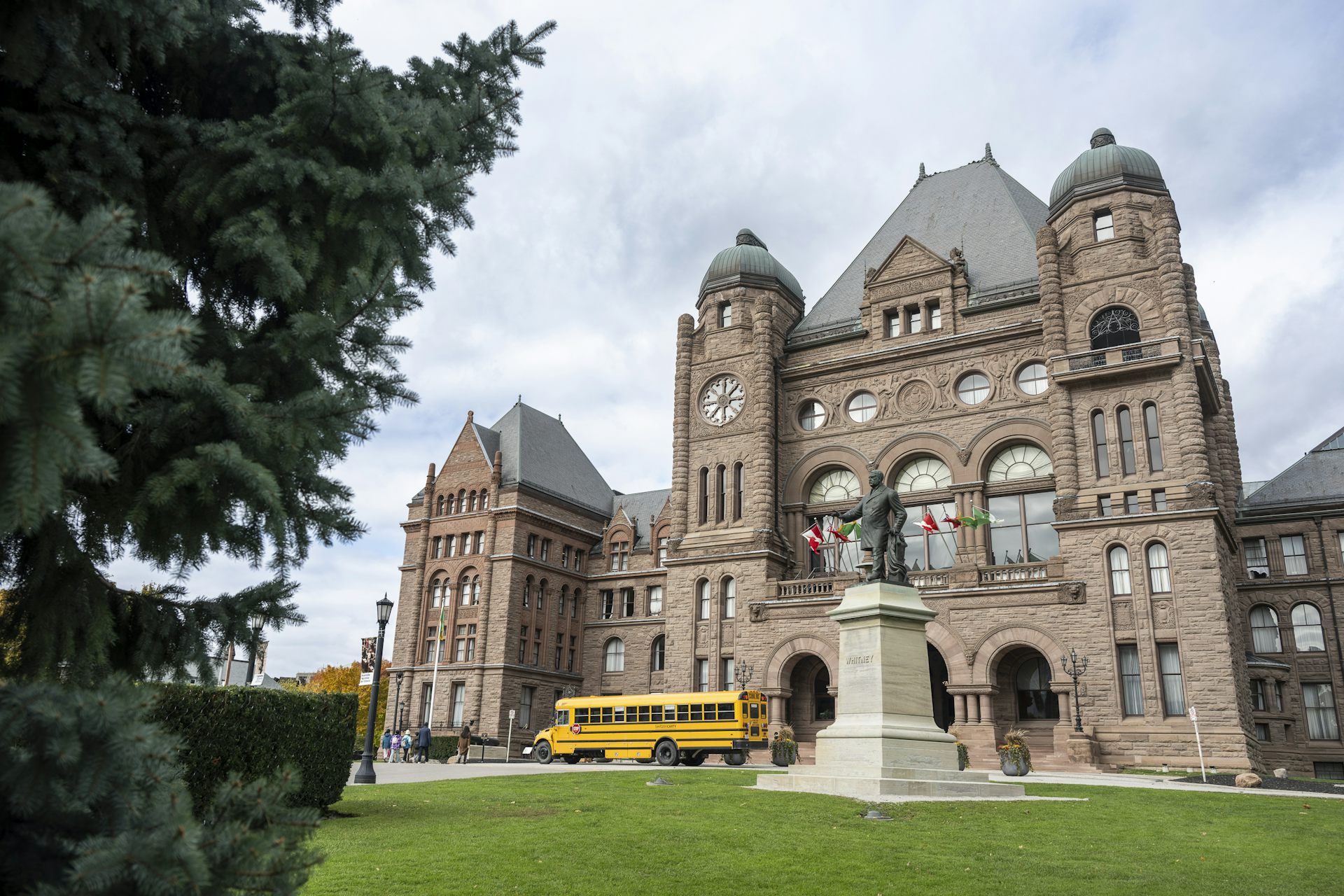 A tall stone building with green peaked roof with school bus and large statue out front. 