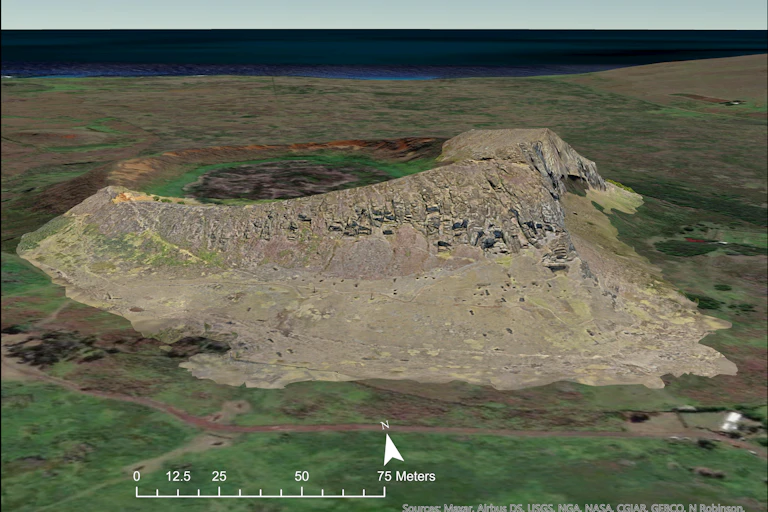 aerial view of a rocky hillside in a treeless landscape with the ocean in the background