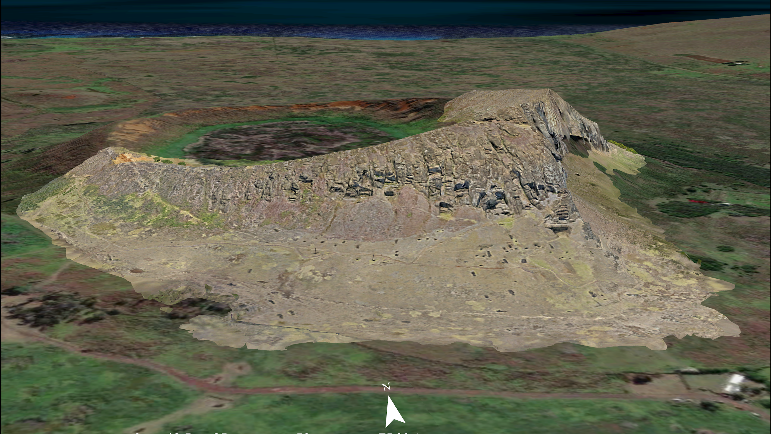 aerial view of a rocky hillside in a treeless landscape with the ocean in the background