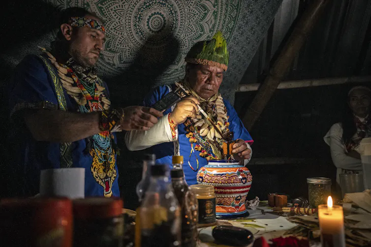 Shaman in colorful outfit and necklaces ladles from a clay pot