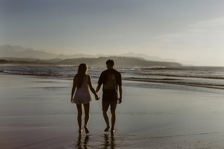Man and woman holding hands walk along a beach.