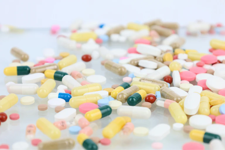 Colourful pink, green, yellow and white pills spilled across a surface.