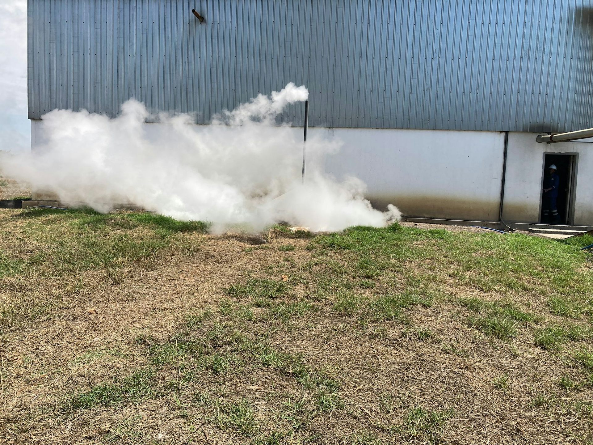 A factory photographed from outside with a pipe sticking up into the air and large amounts of steam pouring out