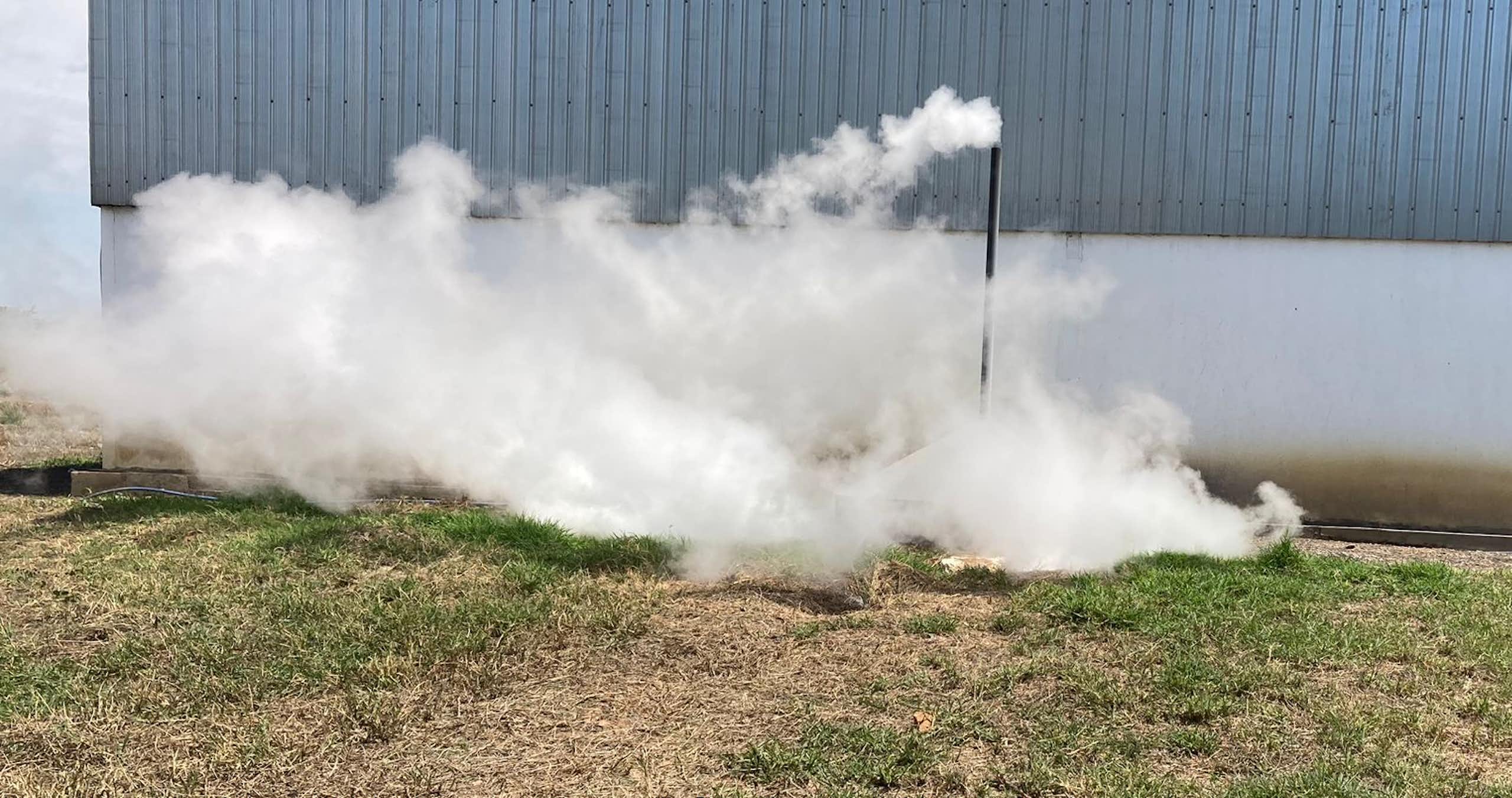 A factory photographed from outside with a pipe sticking up into the air and large amounts of steam pouring out