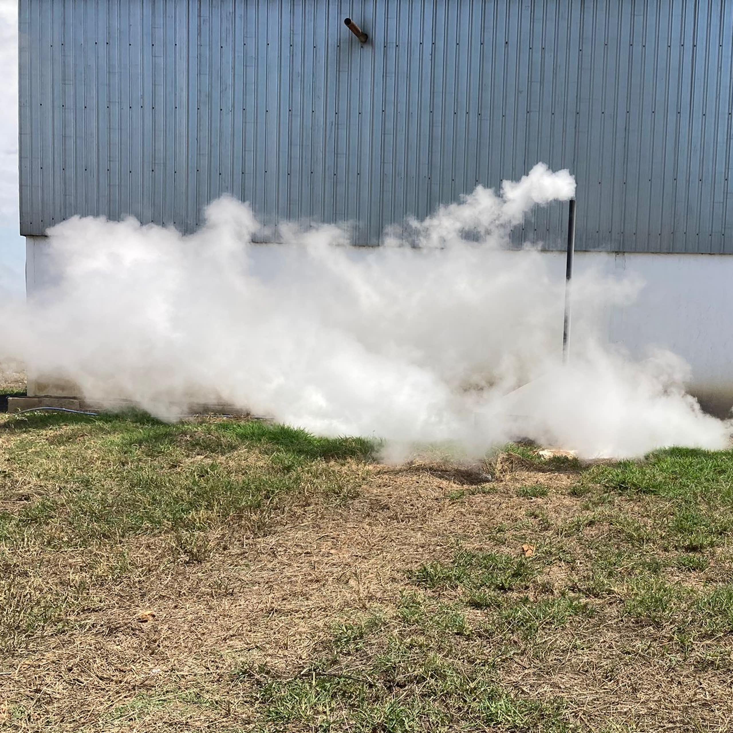 A factory photographed from outside with a pipe sticking up into the air and large amounts of steam pouring out