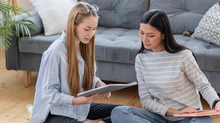 Women sat on floor looking at notebooks together