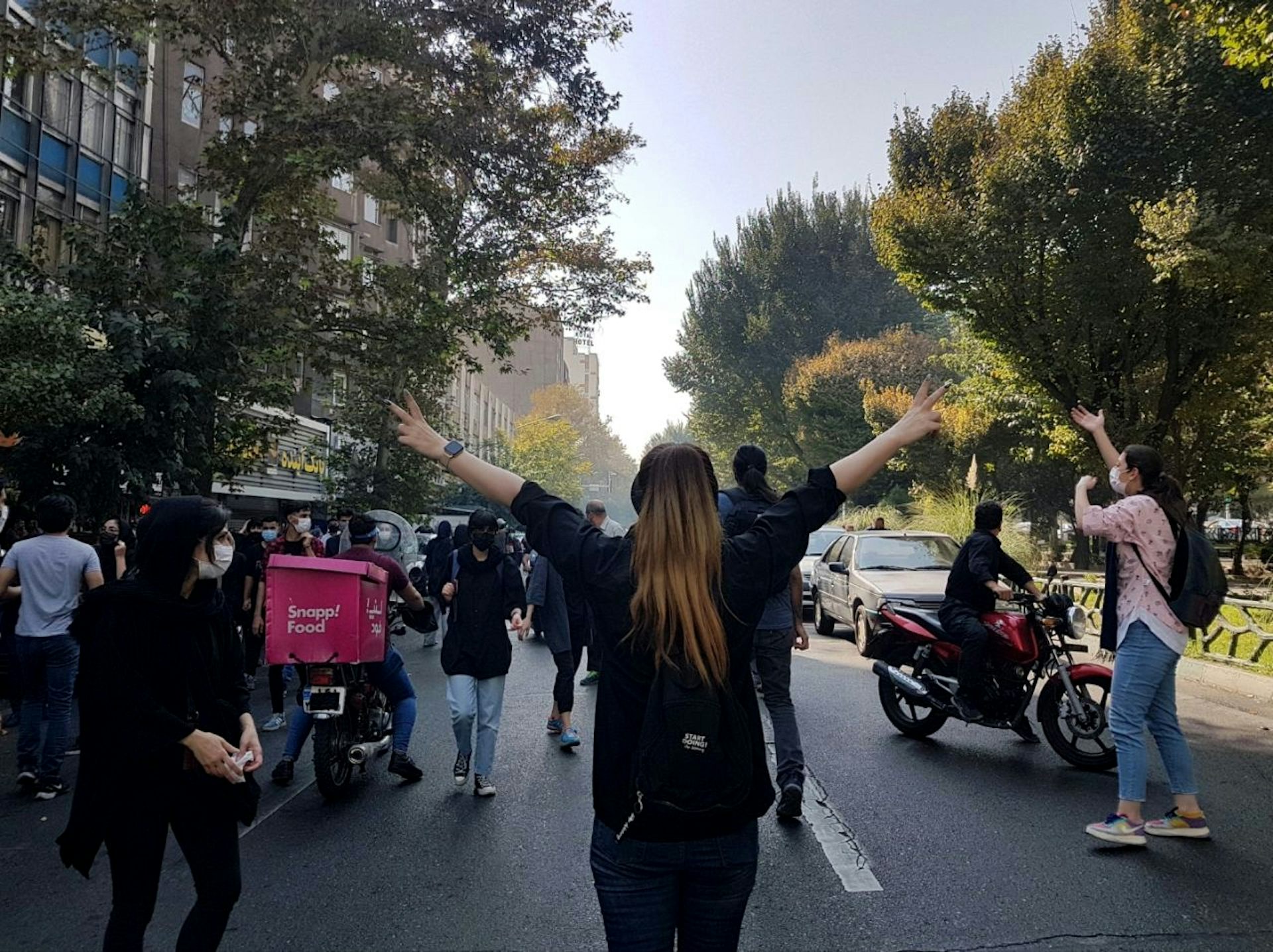 An Iranianwoman protesting in Tehran in 2022 holds her arms in the air. SHe is not wearing a hijab.