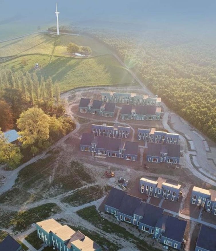 An ariel shot of housing surrounded by fields and a wind turbine.