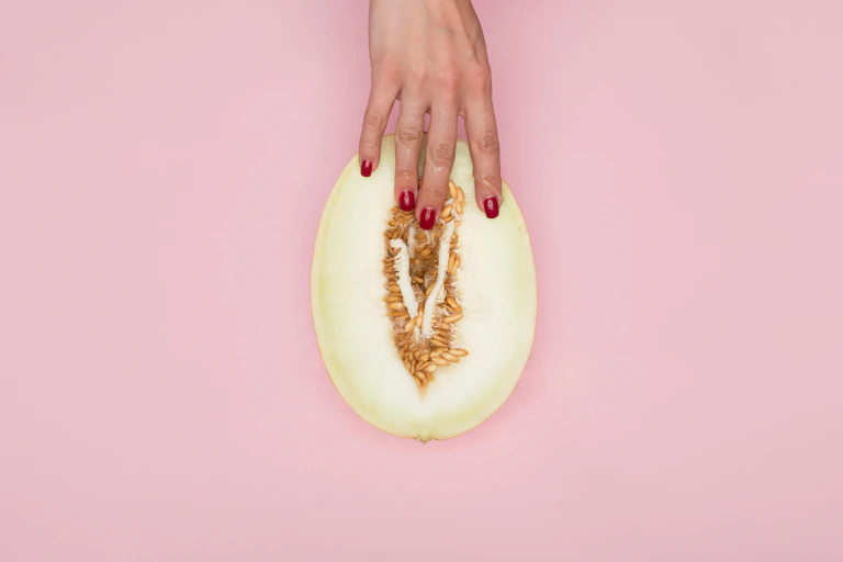 Main de femme tenant un melon, les doigts enfoncés dans la partie charnue.