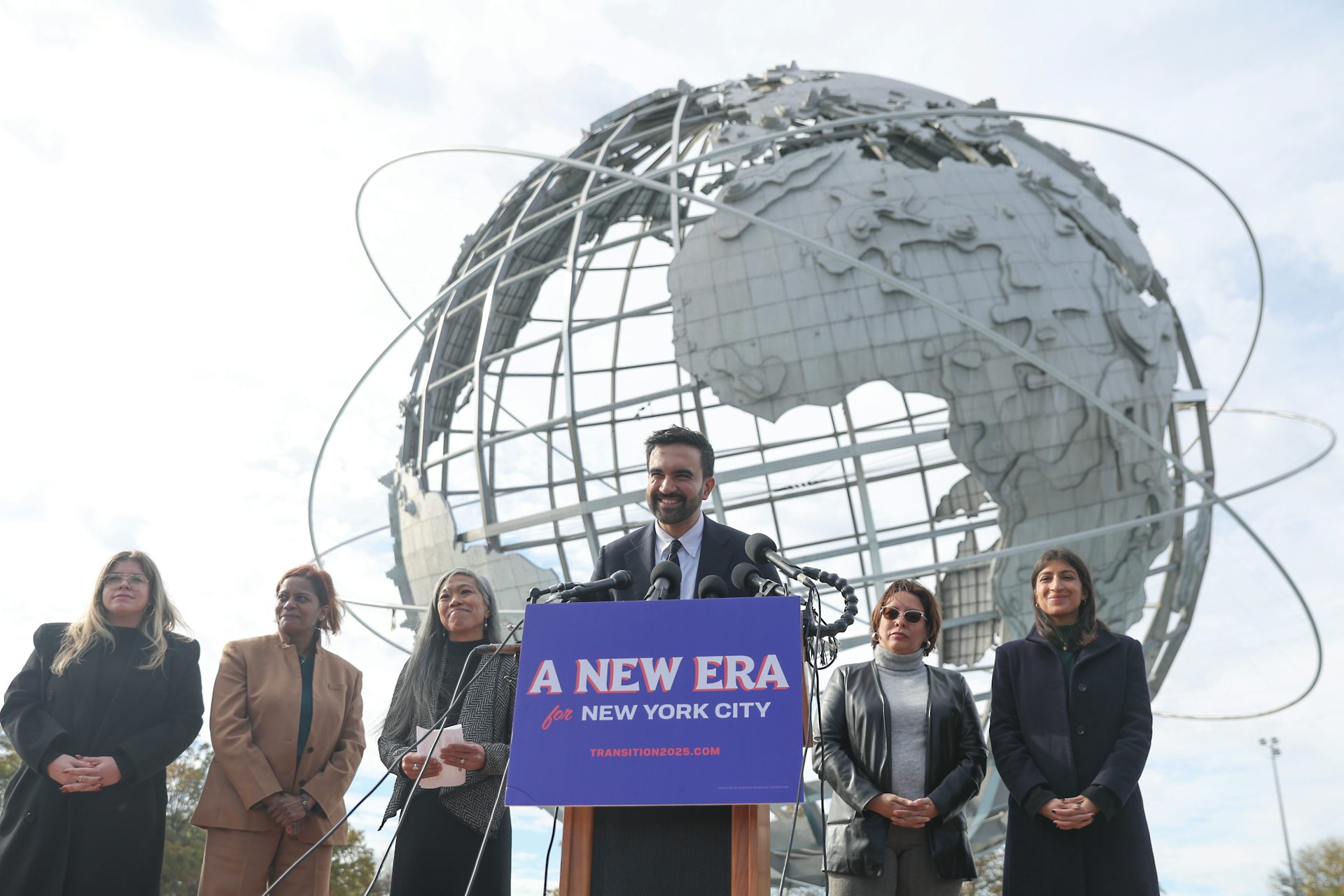People in front of a spheric globe scuplture with a man behind a podium that says 'a new era.'