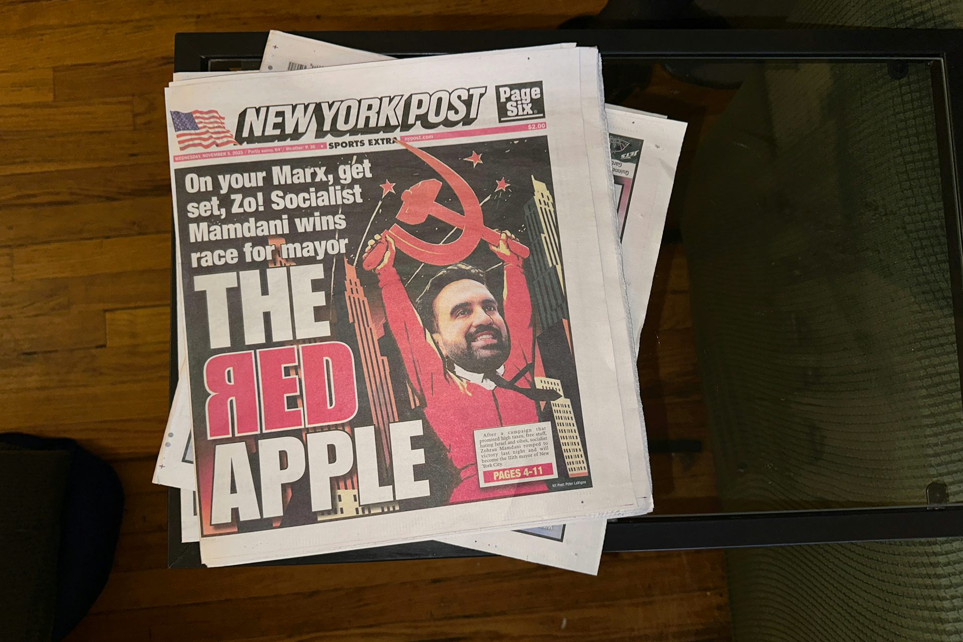 A newspaper shows a picture of a person holding up red sickle and cythe and headline says 'the red apple.'