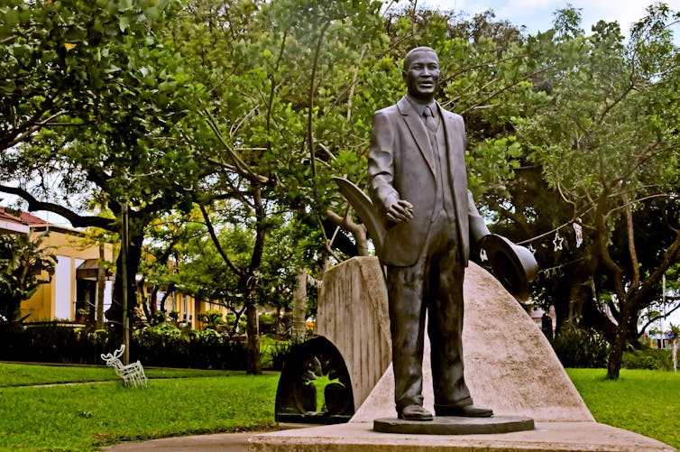 A leafy park with a realistic statue of a black man, dapper in a suit.