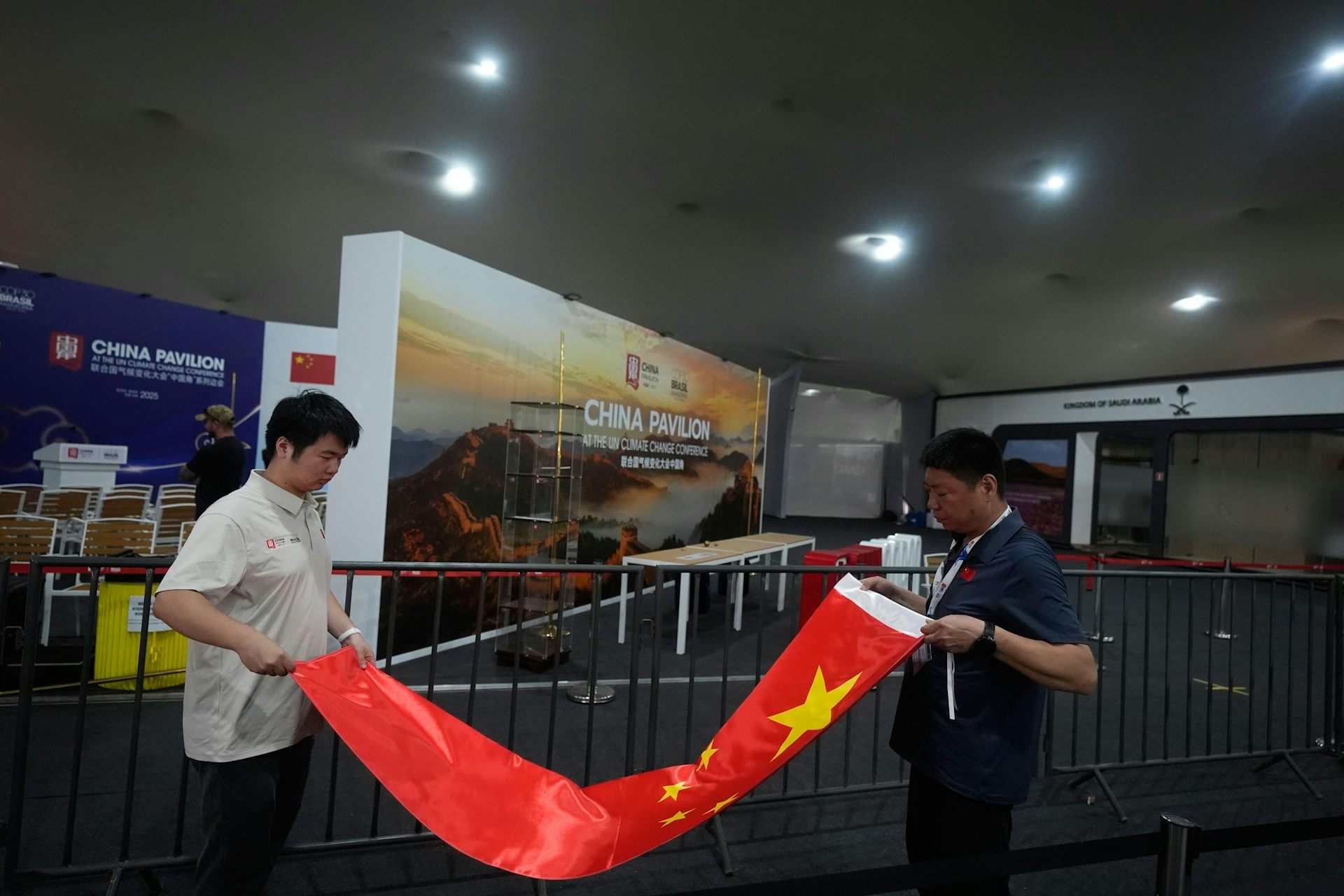 Two men rolling up a Chinese flag in front of the China stand at COP30.